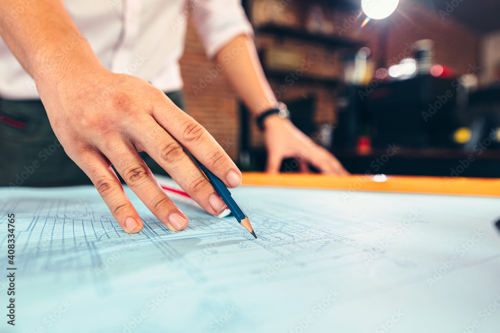 engineers holding a pen pointing to a building and  drawing outlay construction plan as guide for builders with details. Engineer design and writing blueprint.