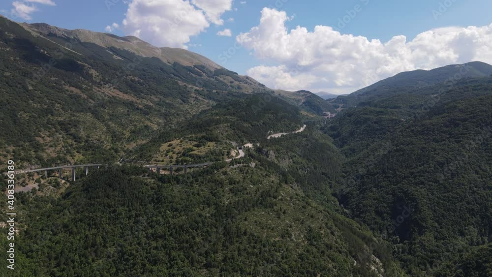 Aerial view of nature in Italian region Abruzzo, with a road high above the ground. The road is surrounded with picturesque green hills. Blue sky with white clouds offers a splendid contrast. Aerial view of nature in Italian region Abruzzo, with a road high above the ground. The road is surrounded with picturesque green hills. Blue sky with white clouds offers a splendid contrast.