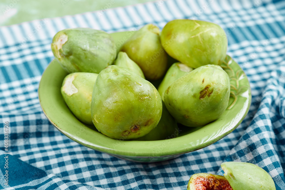 A bowl of juicy green figs and slices of fig on a blue tablecloth A bowl of juicy green figs and slices of fig on a blue tablecloth