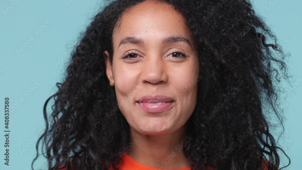 Close up young pretty african woman with curly hair lush hairstyle 20s years old in casual orange sweatshirt looking camera smiling laughing isolated on pastel blue color background studio portrait