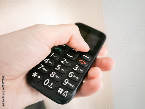 Hand palm holding big push button, simple mobile phone for seniors.