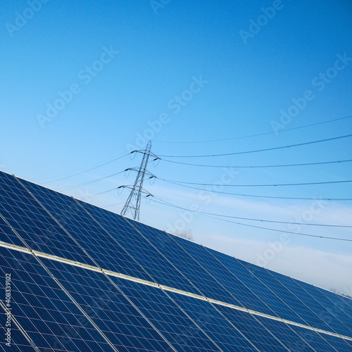 Solar photovoltaic panels generating renewable energy with electricity pylon distribution network in the background. 