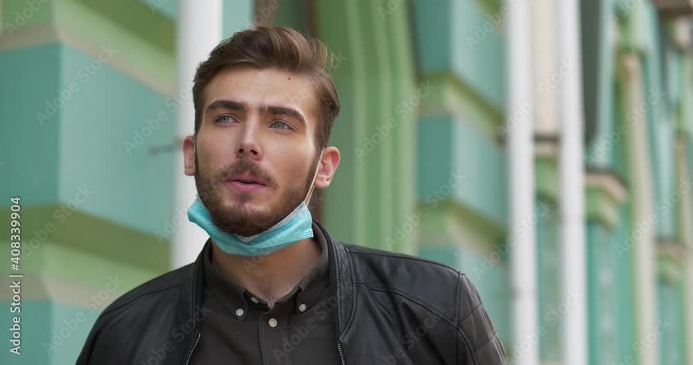Young handsome man in medical protective face mask on the chin smokes a cigarette, then he takes off mask. Cinema 4K 60fps video