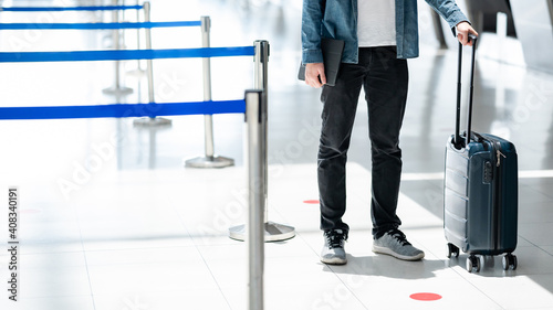 Travel insurance concept. Male tourist carrying suitcase luggage and digital tablet waiting for check in and baggage claim at airline counter in airport terminal.