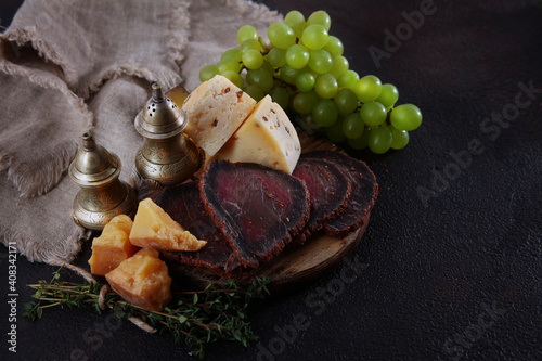Homemade sausage and cold cuts on a black background. Craft cheese and green grapes on a wooden board. Natural products. Vintage spice containers. Wooden boards for serving food.