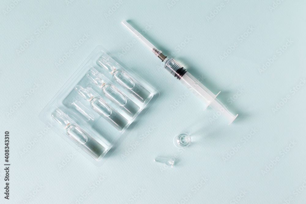 Several doses of vaccine and a syringe with medicine on a blue background. Vaccination. COVID-19, SARS - CoV2 Vaccine concept. Copy space. Horizontal orientation. Top view. Several doses of vaccine and a syringe with medicine on a blue background. Vaccination. COVID-19, SARS - CoV2 Vaccine concept. Copy space. Horizontal orientation. Top view.
