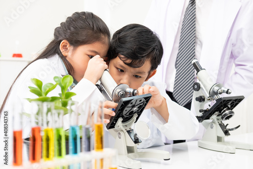 Foto Young Asian kids wearing white scientist gown and do chemical test tube while study, learning in science classroom with teacher