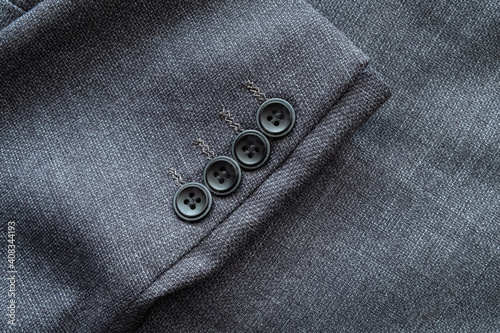 High resolution with details and quality shot of formal black or dark grey wool suit fabric texture. with button decoration under light and shadow ambient. Ideal for background or wallpaper.