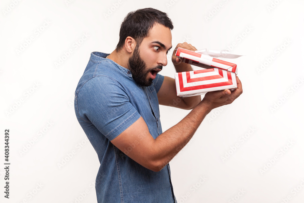 Profile portrait surprised man unpacking giftbox and taking a glance inside, shocked wondered with content Profile portrait surprised man unpacking giftbox and taking a glance inside, shocked wondered with content