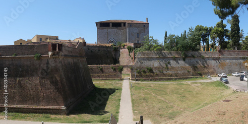 Porta di Santa Lucia of Grosseto is situated along the walls before the Cassero Senese with the black and white symbol of Siena. A stone bastion stands on the left among the green lawn.