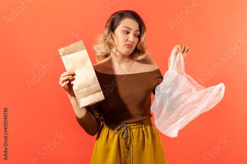 Young woman holding in hands paper and plastic bags, preferring ecological products, campaign against plastic