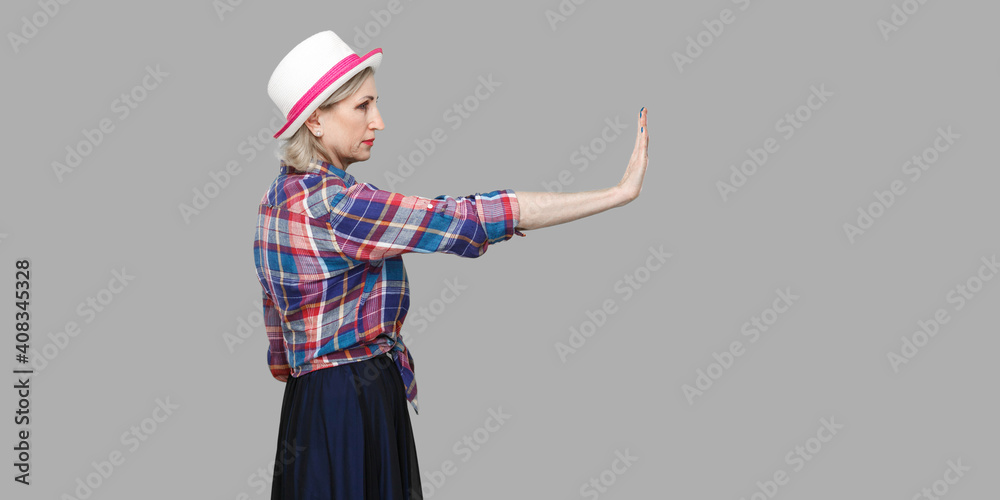 Stop it. Profile side view portrait of serious modern stylish mature woman in casual style with hat standing looking forward and showing stop sign. Stop it. Profile side view portrait of serious modern stylish mature woman in casual style with hat standing looking forward and showing stop sign.