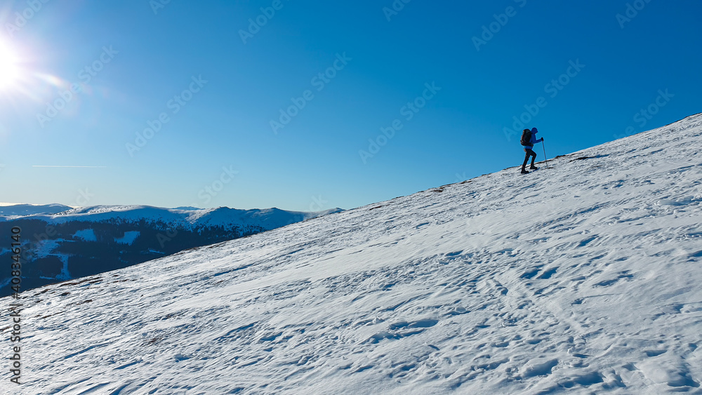 A man wearing snow shoes hiking up along a steep slope to the peak of Speikkogel in Austrian Alps. The whole slope is covered with snow. many mountain chains in the back. Winter outdoor activity.