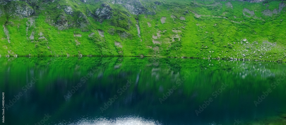 Obraz premium wonderful reflection from green hills in a mountain lake panorama