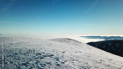 Distant drone shot of a couple wearing snow shoes hiking up to the peak of Speikkogel in Austrian Alps. The whole slope is covered with snow. Many mountain chains in the back. Winter outdoor activity