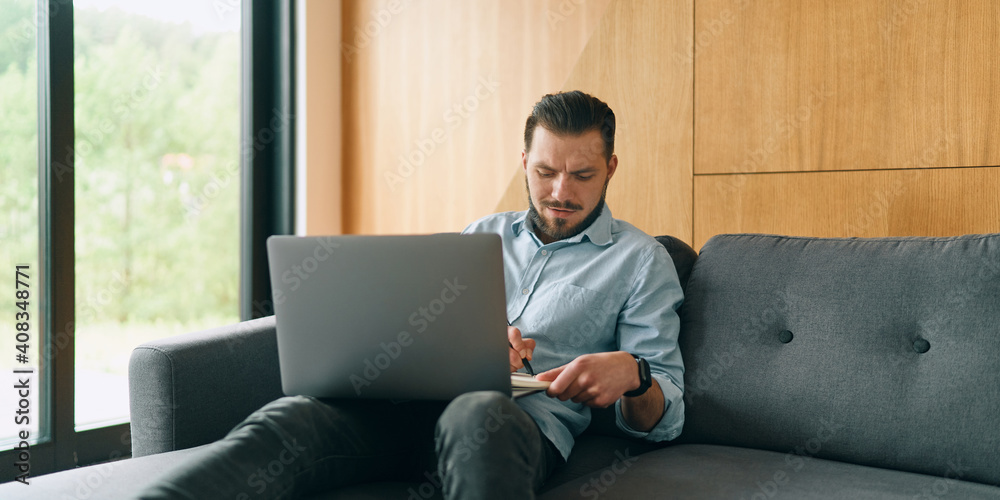 Cheerful businessman using laptop and notebook in cosy home office space Cheerful businessman using laptop and notebook in cosy home office space