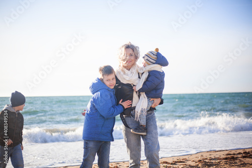 Happy family, mother with sons walking wirh fun in the sea shore on windy day. People dressed warm clothes.