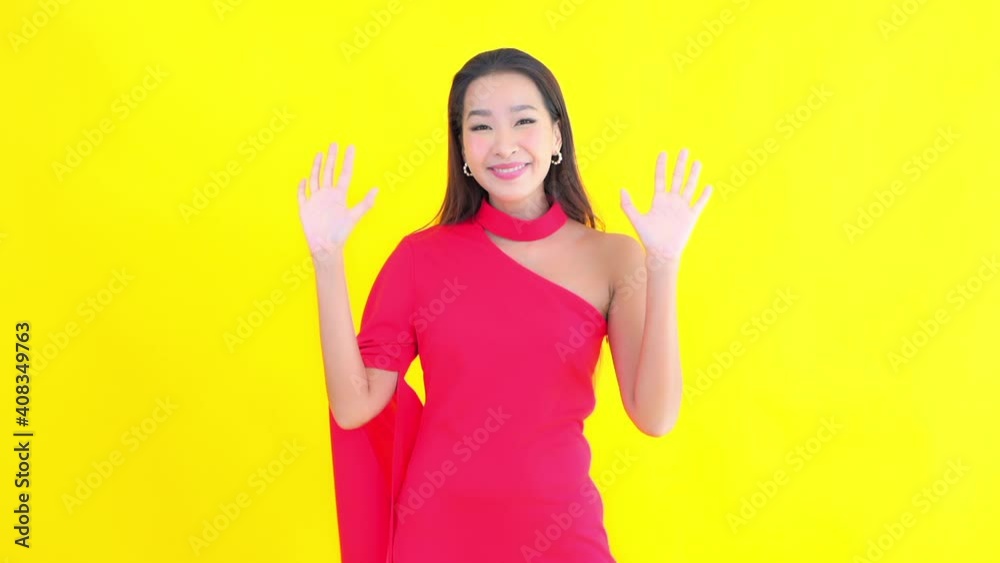 Young Asian woman greets in elegant fuchsia dress with yellow screen in background Young Asian woman greets in elegant fuchsia dress with yellow screen in background