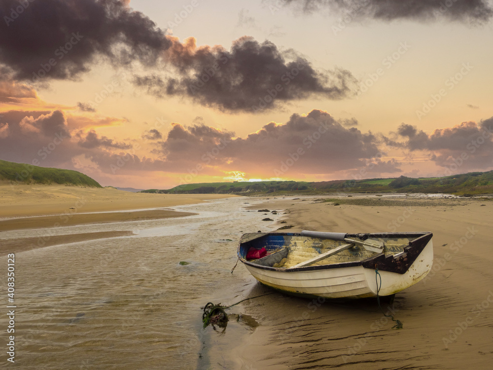 Aberffaw, Anglesey, Wales.  A small boat moored on the beach at Aberffraw with the sun setting.