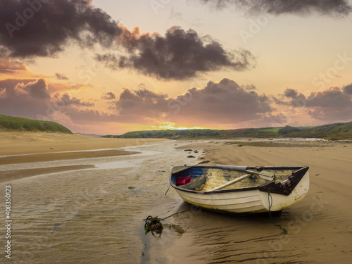 Aberffaw, Anglesey, Wales.  A small boat moored on the beach at Aberffraw with the sun setting.
