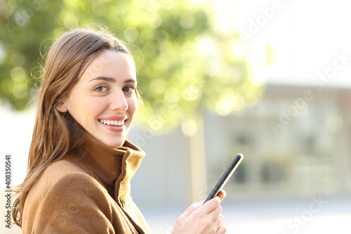 Happy woman holding phone looks at you in winter