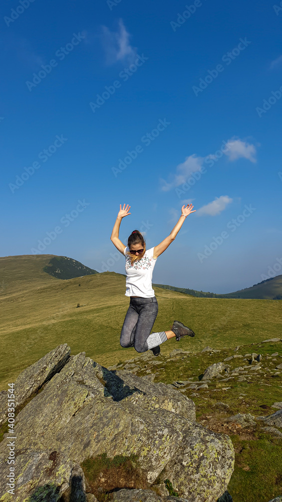 Woman in hiking outfit jumping above a big rock and having fun while hiking to Speikkogel, Austrian Alps. The mountains around are lush green, not so sharp. Sunny summer day. Exploration and discovery Woman in hiking outfit jumping above a big rock and having fun while hiking to Speikkogel, Austrian Alps. The mountains around are lush green, not so sharp. Sunny summer day. Exploration and discovery
