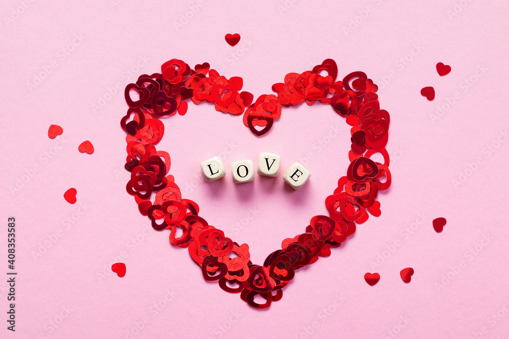 Wooden cubes with the word LOVE in the center heart made by small red hearts on pink background, top view. Valentine's Day background with wooden letter blocks. Love concept. Wooden cubes with the word LOVE in the center heart made by small red hearts on pink background, top view. Valentine's Day background with wooden letter blocks. Love concept.
