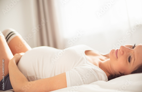 Happy pregnant woman lying down on bed in bright room.
