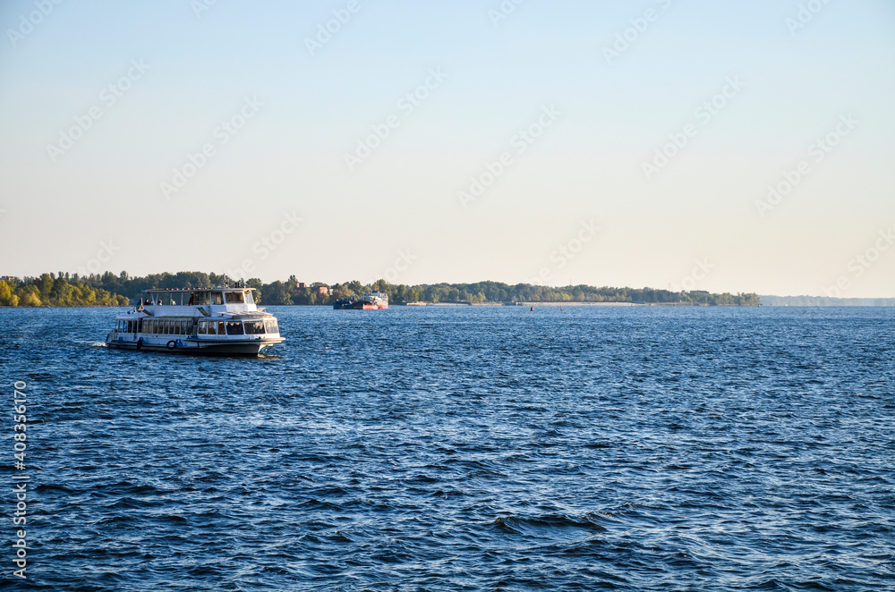 Tourist pleasure boat floats on the river Dnipro in the city Zaporizhya at sunset. Weekend walks.