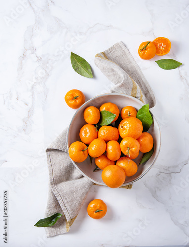 sweet and juicy tangerines in a ceramic bowl with linen napkin on a white marble background © Kufotos