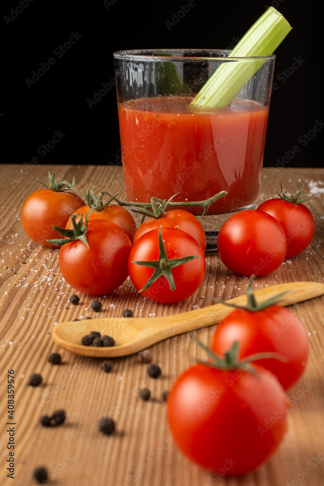 Top view of cherry tomatoes with peppercorns, wooden spoon, glass of tomato juice with celery, selective focus, on wooden table, black background, vertical Top view of cherry tomatoes with peppercorns, wooden spoon, glass of tomato juice with celery, selective focus, on wooden table, black background, vertical
