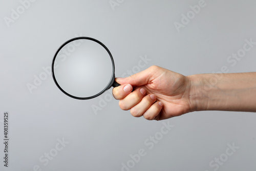 Woman holding magnifying glass on grey background, closeup. Find keywords concept