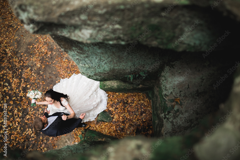 Obraz premium Romantic, fairytale, happy newlywed couple hugging and kissing in a park, trees in background