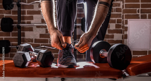 Fitness motivation and muscle training concept. Man in sneakers tying shoelaces in sunlight. Athlete starting exercise with dubbell weight. photo