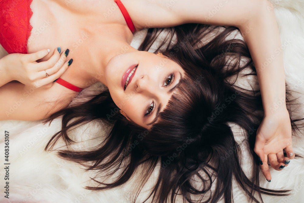 Naklejka premium Sexy brunette in red lingerie lies on the white carpet and smiles