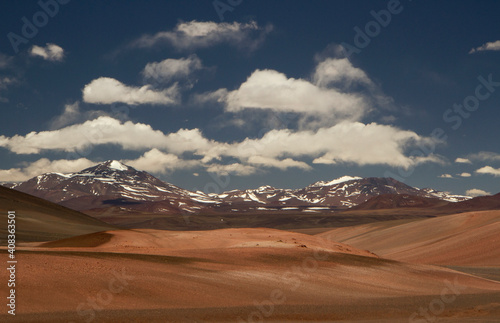Enchanting alpine landscape. View of the desert dunes, sand and Andes mountain range under a magical blue sky with clouds. 