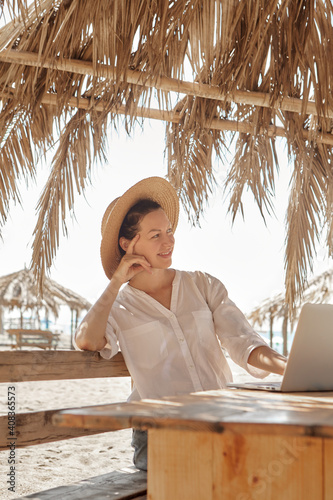 Young woman using laptop computer on a beach. Freelance work concept..Pretty young woman using laptop in cafe on tropical beach in outdoor cafe. Work and travel