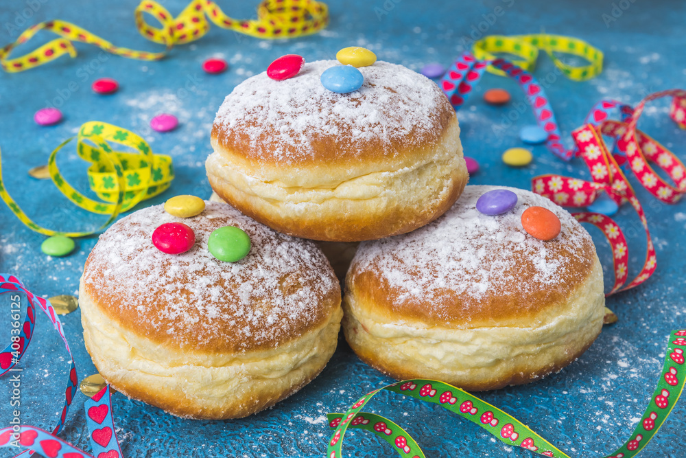 Krapfen, Berliner or donuts with streamers, confetti and chocolate beans on blue background. Colorful carnival or birthday image.