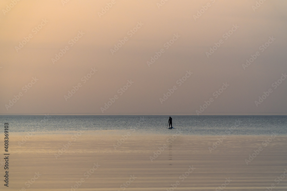 A man with an oar swims standing on a board on the Gulf of Finland.