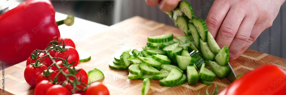 Close up of cook slicing a cucumber on a chopping board while cooking in the kitchen. Healthy homemade food concept