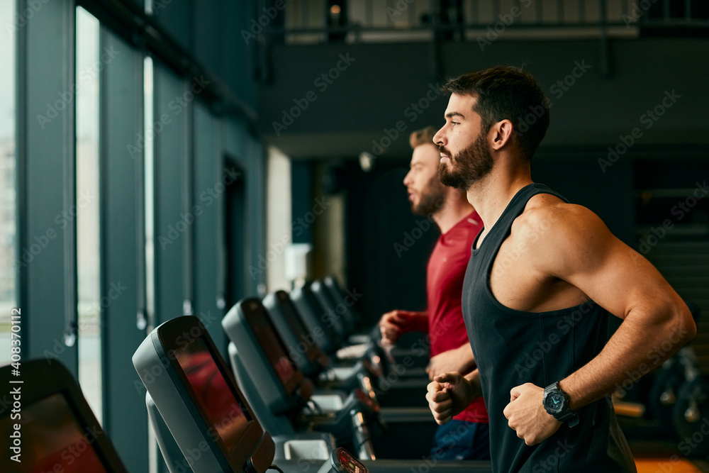 Two young man running on treadmill at gym Two young man running on treadmill at gym