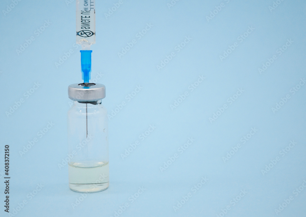 Glass bottle of liquid and syringe on blue background with copy space. Concept of vaccination, coronavirus, Covid-19, treatment of pneumonia with injections of antibiotics. Glass bottle of liquid and syringe on blue background with copy space. Concept of vaccination, coronavirus, Covid-19, treatment of pneumonia with injections of antibiotics.
