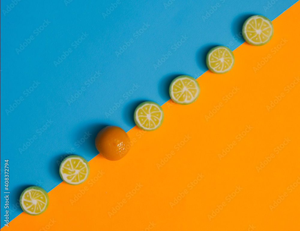 Candy hard bonbon sliced lime fruits aligned in diagonal against pastel blue and orange flat lay composition. Marzipan orange candy in between those hard bonbons. Candy hard bonbon sliced lime fruits aligned in diagonal against pastel blue and orange flat lay composition. Marzipan orange candy in between those hard bonbons.
