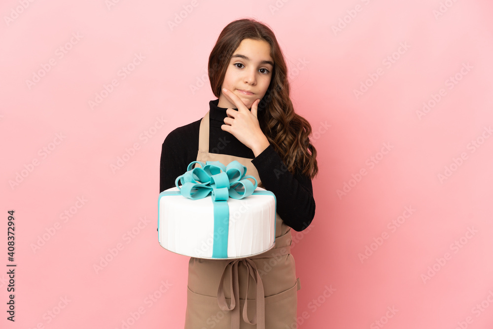 Little Pastry chef holding a big cake isolated on pink background thinking Little Pastry chef holding a big cake isolated on pink background thinking