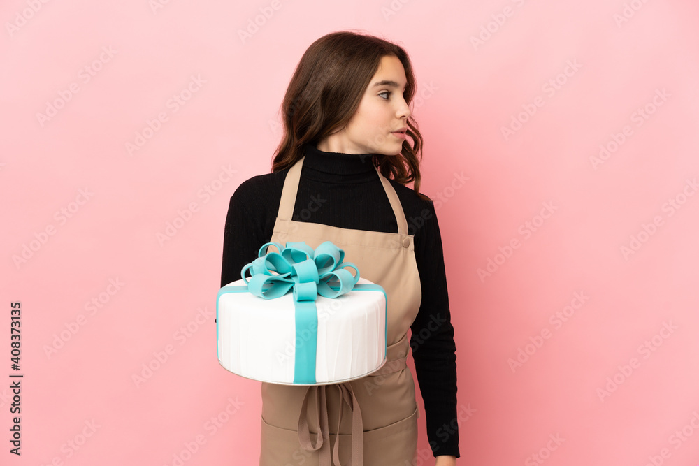 Little Pastry chef holding a big cake isolated on pink background looking to the side Little Pastry chef holding a big cake isolated on pink background looking to the side