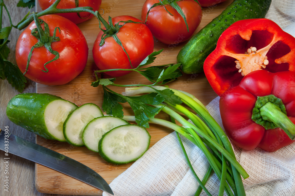 Fresh juicy ripe useful vegetables for salad: red tomatoes, cucumbers, peppers, green onions and parsley on a wooden background. Cutting vegetables on the kitchen blackboard.