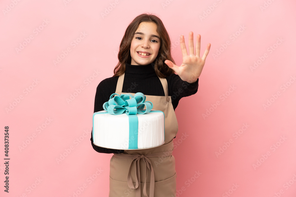 Little Pastry chef holding a big cake isolated on pink background counting five with fingers Little Pastry chef holding a big cake isolated on pink background counting five with fingers