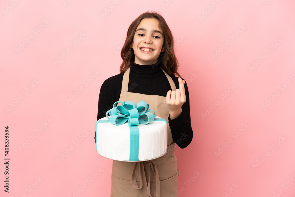 Little Pastry chef holding a big cake isolated on pink background making money gesture Little Pastry chef holding a big cake isolated on pink background making money gesture