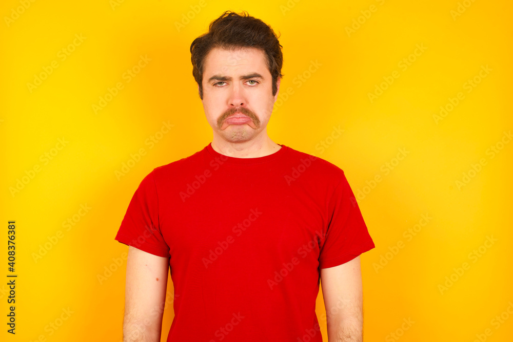 Displeased upset Young Caucasian man wearing red t-shirt standing against yellow wall frowns face as going to cry, being discontent and unhappy as can't achieve goals, Disappointed model has troubles Displeased upset Young Caucasian man wearing red t-shirt standing against yellow wall frowns face as going to cry, being discontent and unhappy as can't achieve goals, Disappointed model has troubles