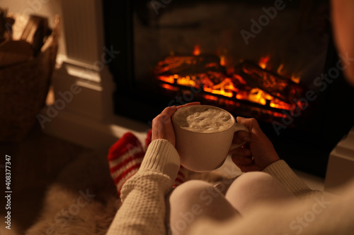 Obraz na plátně Woman holding drink near fireplace with burning woods indoors, closeup